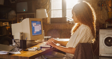 Poster - Side View Of Hispanic Female Software Engineer Programming on Old Desktop Computer In Retro Garage. Focused Woman Starting Tech Startup Company In Nineties. Coding Innovative Online Service At Home.