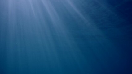 Wall Mural - Underwater sunrays in blue Ocean, Slow motion. The sun's rays penetrate underwater into blue water through sea surface. Diagonal sunbeams under water. 