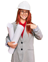 Poster - Young redhead architect woman wearing safety helmet holding blueprints pointing finger to one self smiling happy and proud