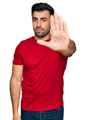 Wall Mural - Hispanic man with beard wearing casual red t shirt doing stop sing with palm of the hand. warning expression with negative and serious gesture on the face.