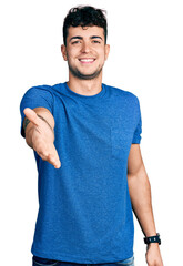 Sticker - Young hispanic man wearing casual t shirt smiling cheerful offering palm hand giving assistance and acceptance.