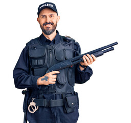 Poster - Young handsome man wearing police uniform holding shotgun looking positive and happy standing and smiling with a confident smile showing teeth