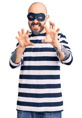 Canvas Print - Young handsome man wearing burglar mask smiling funny doing claw gesture as cat, aggressive and sexy expression