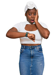 Poster - Young african woman with turban wearing hair turban over isolated background looking at the watch time worried, afraid of getting late