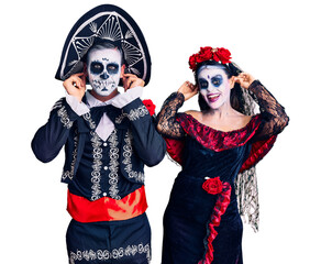 Canvas Print - Young couple wearing mexican day of the dead costume over background smiling pulling ears with fingers, funny gesture. audition problem