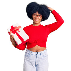 Wall Mural - Young african american girl holding gift confuse and wondering about question. uncertain with doubt, thinking with hand on head. pensive concept.