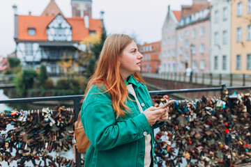 Wall Mural - Sad angry girl standing on city street. Negative people emotion, Urban lifestyle concept. Upset young woman is using a smartphone in park outdoors, autumn time.