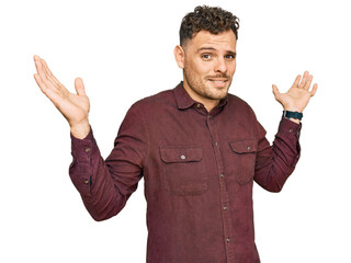 Canvas Print - Young hispanic man wearing casual clothes clueless and confused expression with arms and hands raised. doubt concept.