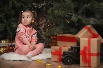 Wall Mural - Little girl in new year's Christmas atmosphere. The girl is happy with Christmas and gifts. A child at the New Year tree with gifts.