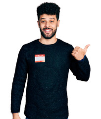 Poster - Young arab man with beard wearing hello my name is sticker identification pointing thumb up to the side smiling happy with open mouth