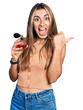 © Krakenimages.com - Hispanic young woman holding perfume pointing thumb up to the side smiling happy with open mouth