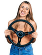 © Krakenimages.com - Hispanic young woman holding steering wheel smiling with a happy and cool smile on face. showing teeth.