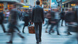 A businessman with a full-length briefcase stands in the middle of the street around a blurred group of people walking fast