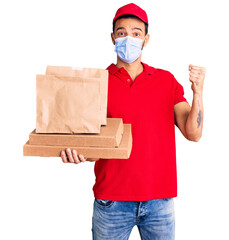 Wall Mural - Young handsome hispanic man delivering food wearing covid-19 safety mask screaming proud, celebrating victory and success very excited with raised arms