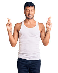 Wall Mural - Young hispanic man wearing casual clothes gesturing finger crossed smiling with hope and eyes closed. luck and superstitious concept.