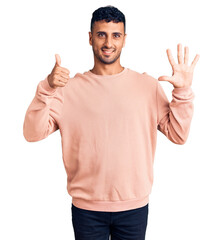 Wall Mural - Young hispanic man wearing casual clothes showing and pointing up with fingers number six while smiling confident and happy.