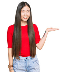 Sticker - Young chinese woman wearing casual clothes smiling cheerful presenting and pointing with palm of hand looking at the camera.