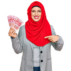 Poster - Beautiful hispanic woman wearing islamic hijab holding chinese yuan banknotes pointing finger to one self smiling happy and proud