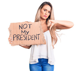 Poster - Young beautiful blonde woman holding not my president cardboard banner with angry face, negative sign showing dislike with thumbs down, rejection concept