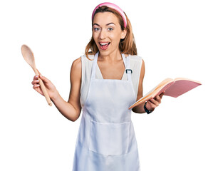 Sticker - Young caucasian woman wearing professional baker apron reading cooking recipe book celebrating crazy and amazed for success with open eyes screaming excited.