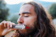 a young man with long hair plays the harmonica. a man enjoys playing the harmonica.
