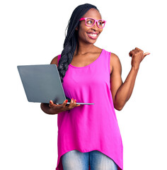 Wall Mural - Young african american woman working using computer laptop pointing thumb up to the side smiling happy with open mouth