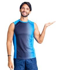 Poster - Handsome hispanic man wearing sportswear smiling cheerful presenting and pointing with palm of hand looking at the camera.