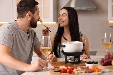 Wall Mural - Affectionate couple enjoying cheese fondue during romantic date in kitchen