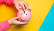 Kids hands with pink Piggy bank isolated on colored background. Pink piggy bank on yellow blue background, financial literacy. Money investment, creative business concept. Safe finance investment