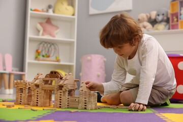 Sticker - Little boy playing with wooden construction set on puzzle mat in room. Child's toy