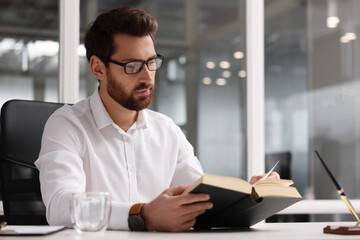 Poster - Handsome man reading book at table in office, space for text. Lawyer, businessman, accountant or manager