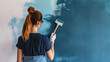 A young woman paints a wall with a paint roller. Portrait of a beautiful woman painting a wall with blue paint in an apartment. Repair concept.