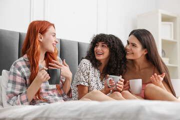 Sticker - Happy young friends with cups of drink on bed at home