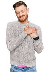 Wall Mural - Young redhead man wearing casual winter sweater smiling with hands on chest with closed eyes and grateful gesture on face. health concept.