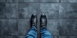 Close-up of person standing on tiled floor in black shoes and blue jeans