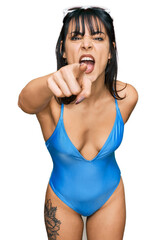 Wall Mural - Young hispanic woman wearing swimsuit and sunglasses pointing displeased and frustrated to the camera, angry and furious with you