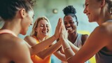 Fototapeta  - Group of diverse fitness friends putting their hands together in a huddle before a yoga session. People supporting each other in a community wellness centre.