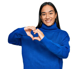 Wall Mural - Young asian woman wearing casual winter sweater smiling in love showing heart symbol and shape with hands. romantic concept.