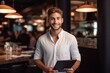 Young sympathetic successful man holding laptop in nice restaurant and smiling 