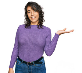 Wall Mural - Young hispanic woman wearing casual clothes smiling cheerful presenting and pointing with palm of hand looking at the camera.