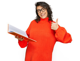 Sticker - Young hispanic woman reading a book wearing glasses smiling happy and positive, thumb up doing excellent and approval sign