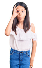 Canvas Print - Beautiful child girl wearing casual clothes doing ok gesture shocked with surprised face, eye looking through fingers. unbelieving expression.