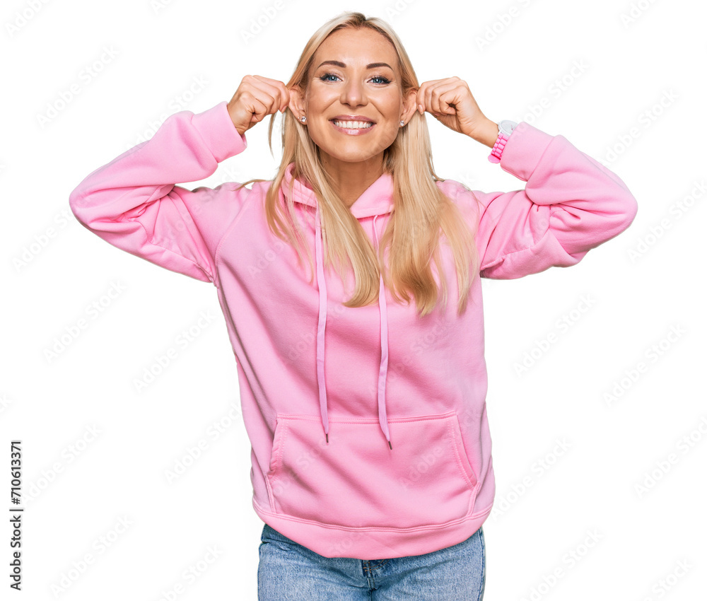 Young blonde woman wearing casual sweatshirt smiling pulling ears with fingers, funny gesture. audition problem