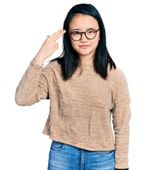 Wall Mural - Young chinese woman wearing casual sweater and glasses shooting and killing oneself pointing hand and fingers to head like gun, suicide gesture.