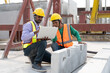© Supachai - Asian male civil engineers wearing vest and helmet safety discussing foreman worker at construction site. Indian foreman with laptop working at factory making precast concrete wall.