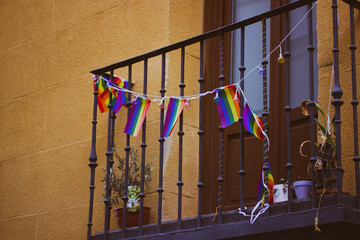 A balcony decorated with rainbow garland of LGBT flags. Cozy orange home. House exterior details. Pride month in Europe. Gay community neighborhood .