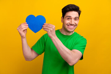 Sticker - Photo portrait of handsome young brunet guy hold blue heart postcard dressed stylish green outfit isolated on yellow color background