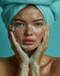 Mujer de mediana edad con toalla en la cabeza, cabello recogido, realiza tratamiento cuidado facial con gel exfoliante. fondo azul aguamarina, turquesa, piel radiante tersa, luminosa, 