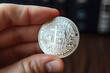 Close-up of a hand holding a silver Bitcoin token with blurred background.