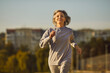 © Studio Romantic - Happy beautiful smiling senior woman in sports clothes running on a city street during her outdoor fitness workout in the summer. Old age, healthy lifestyle, exercise concept